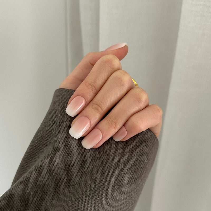 A hand with press-on nails featuring a square shape and a nude ombre color gradient.