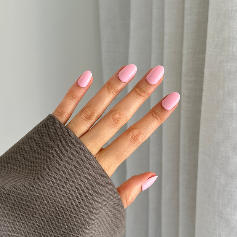 A hand with pink oval-shaped gel press on nails on a neutral background with a grey sleeve.