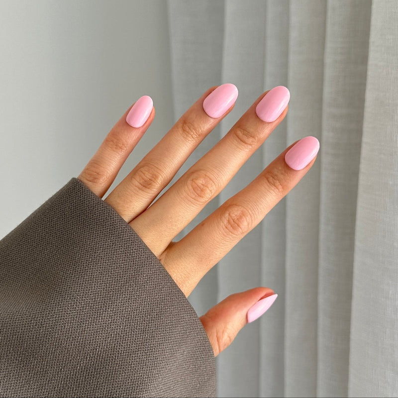 A hand with pink oval-shaped gel press on nails on a neutral background with a grey sleeve.