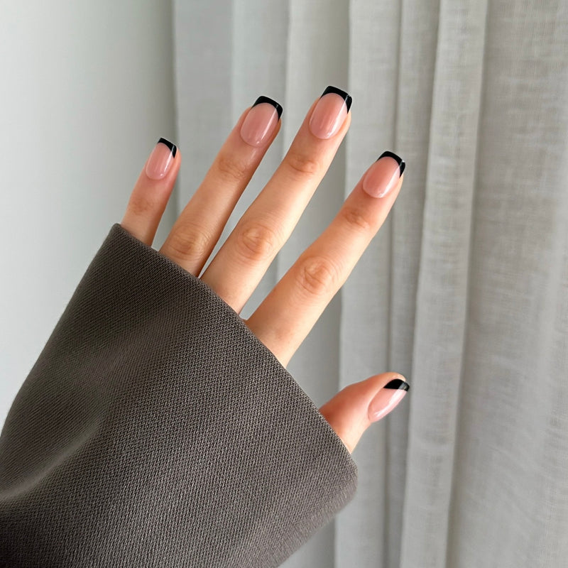 Hand with black french press on nails against a white curtain background