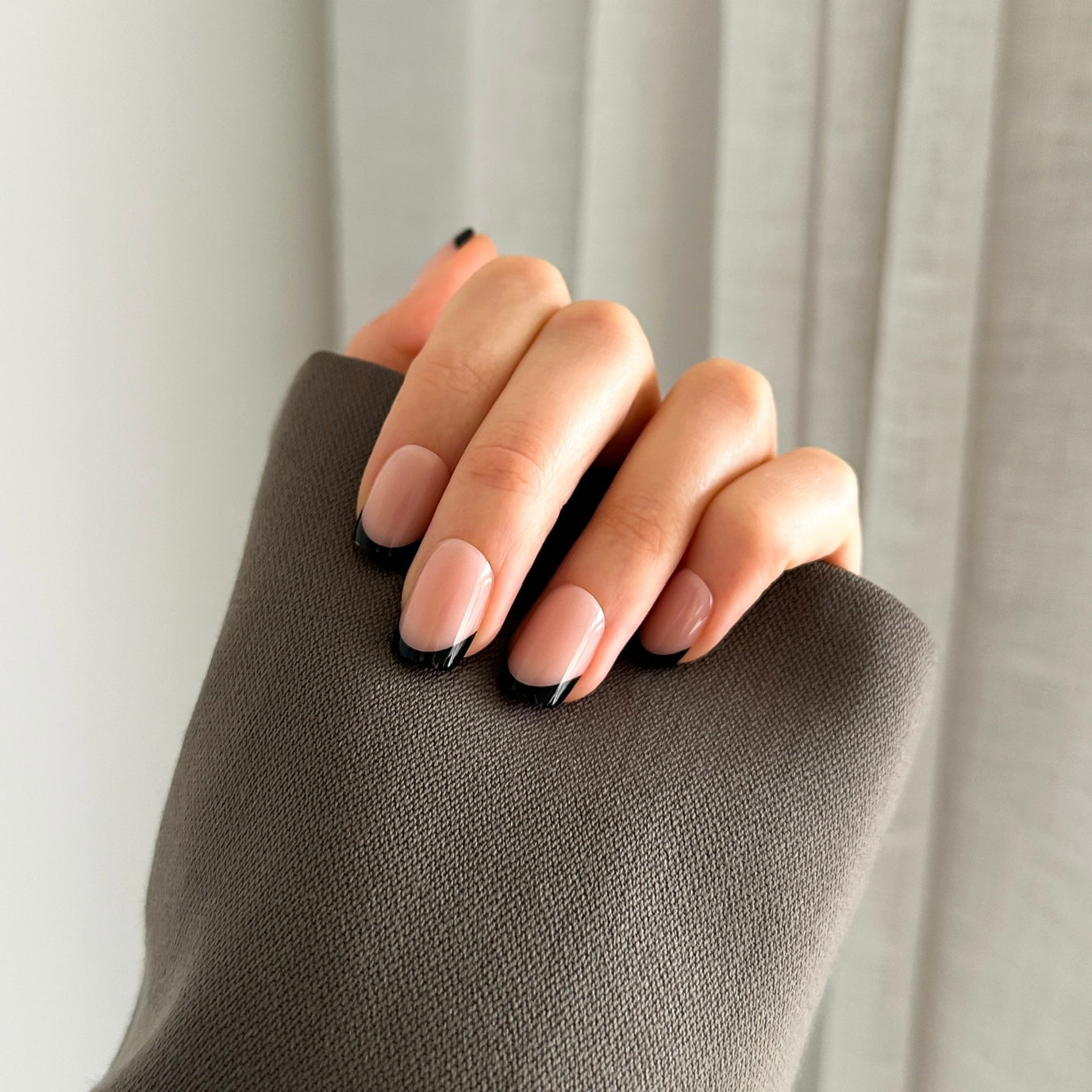 Hand with black french press on nails against a white curtain background