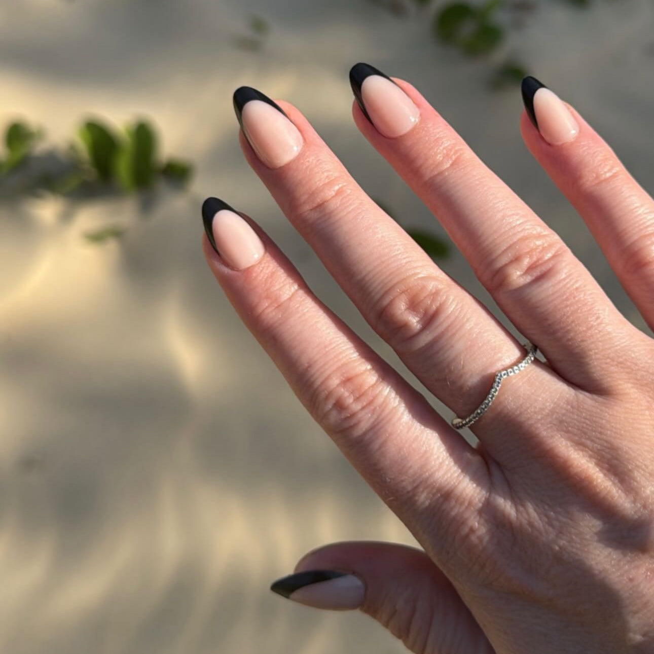 Hand with black and white press on nails against a blurred natural background