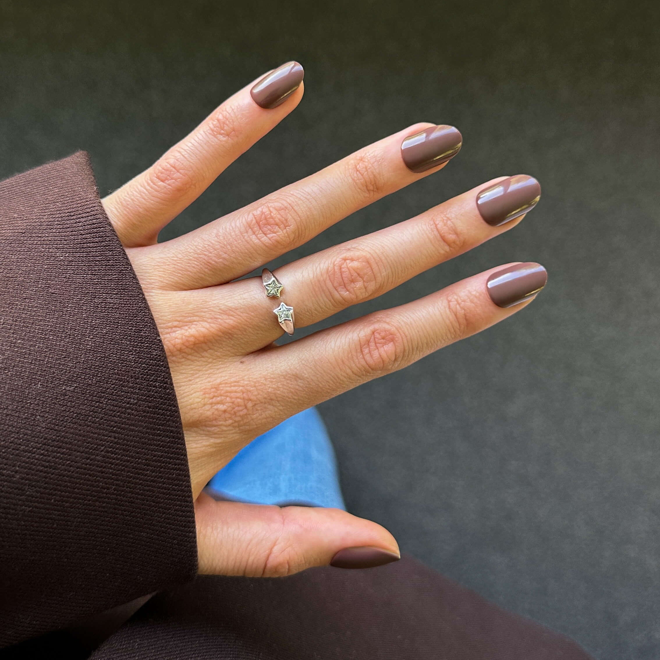 Hand with brown press on nails wearing a ring, against a blurred background