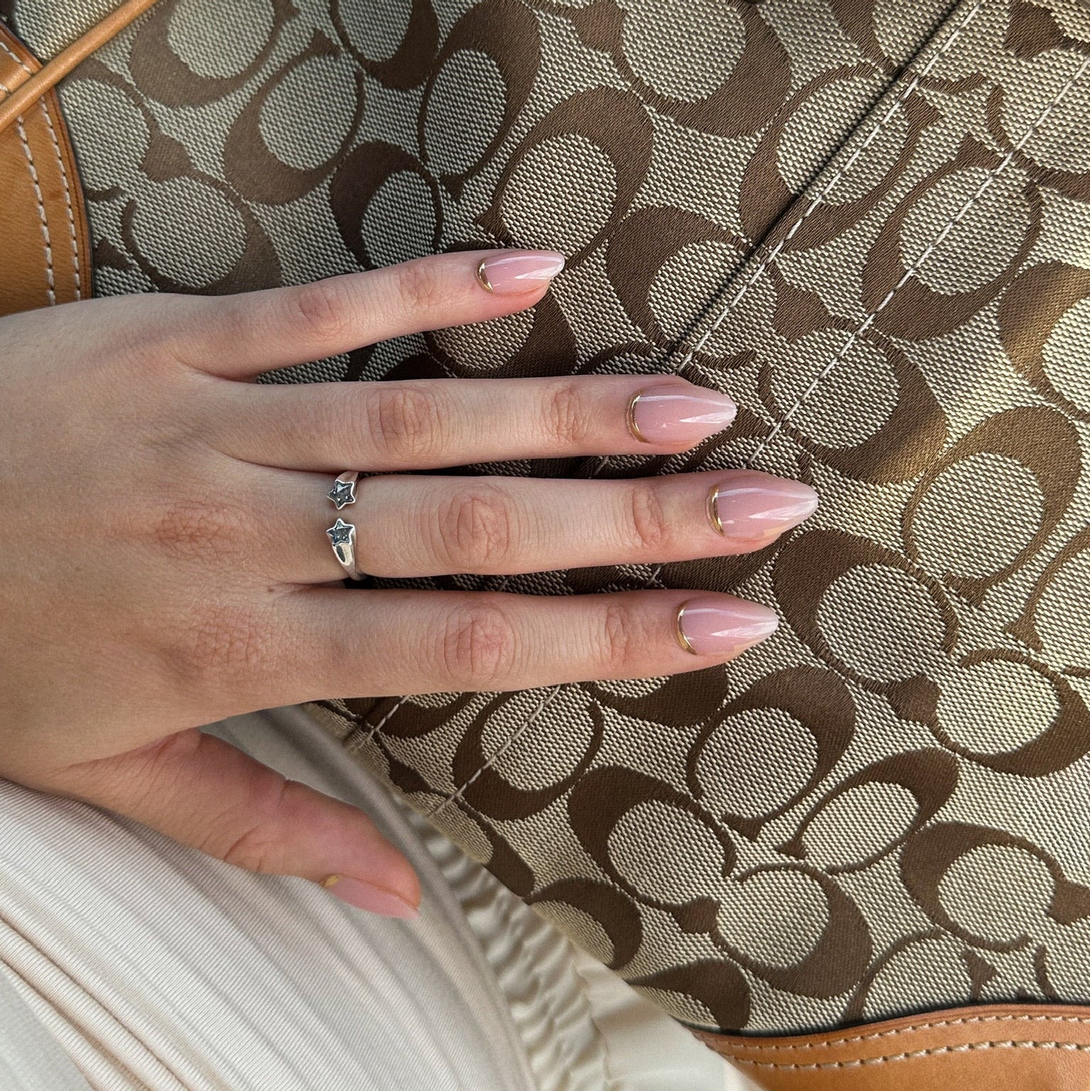 Hand with press on nails wearing a ring on a Coach handbag