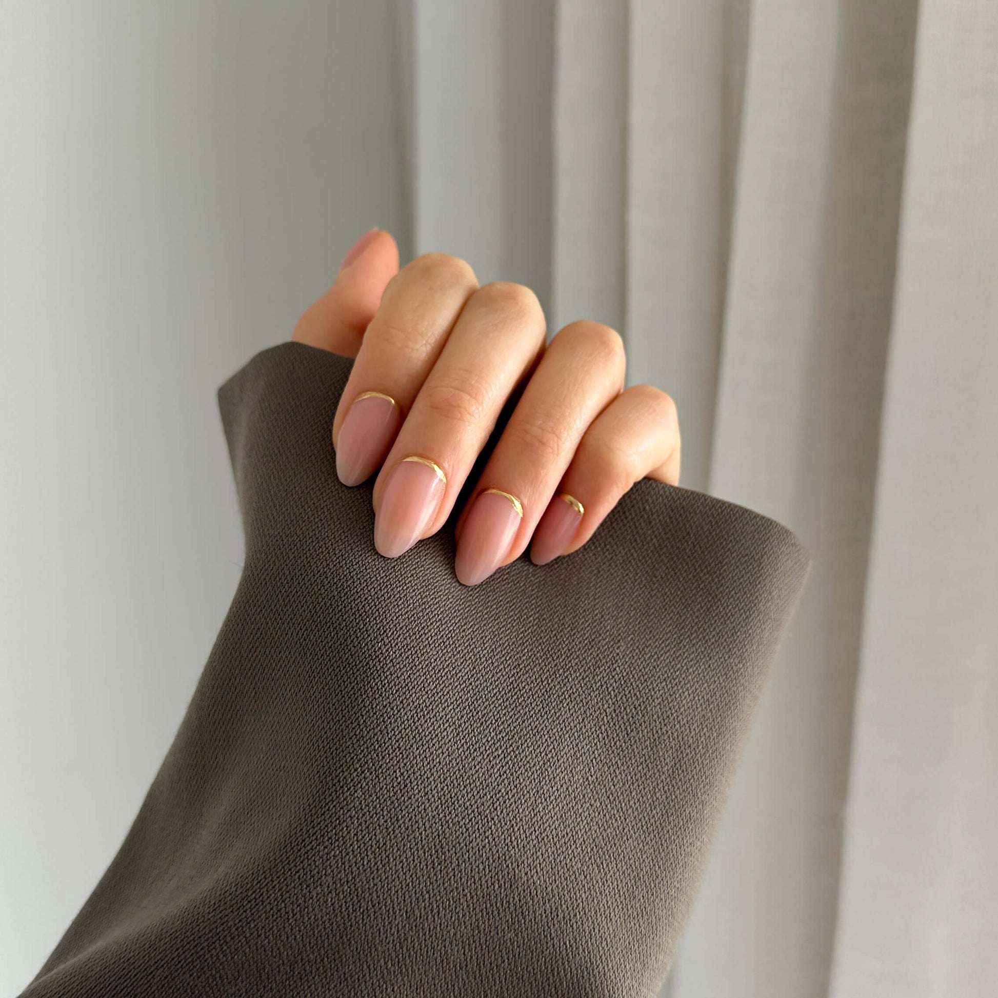 A person's hand with press-on nails showing a natural nail color.