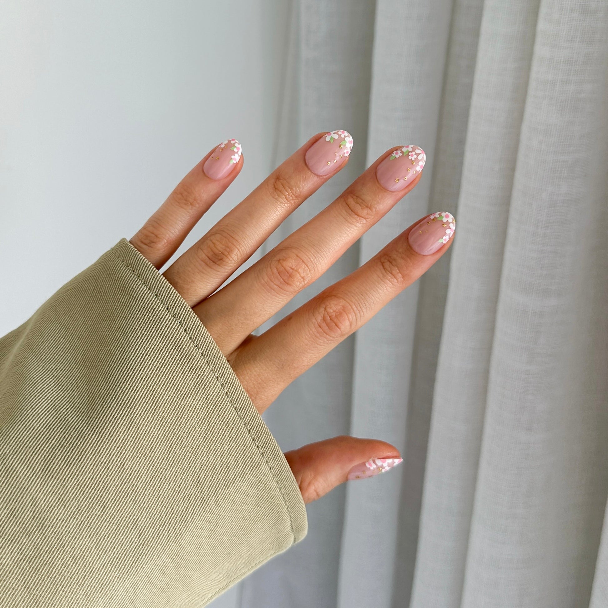 A hand displaying press-on nails with a beige nail polish and daisy designs on a light background.