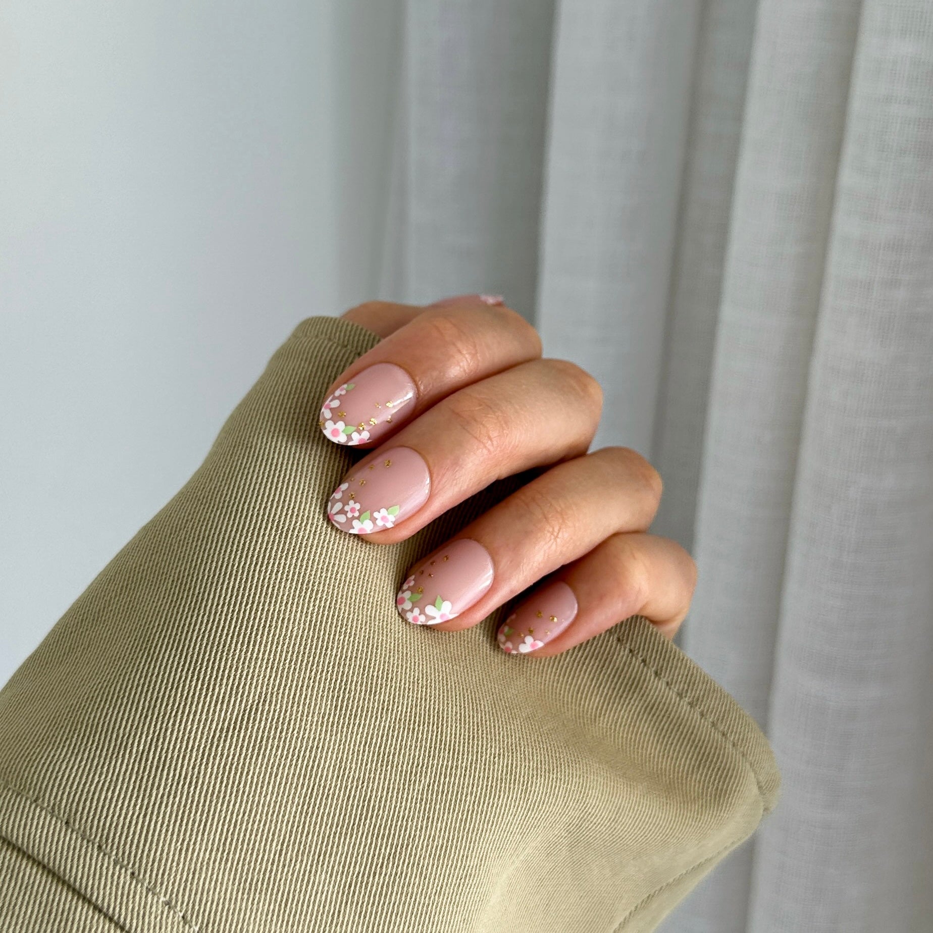 A hand displaying press-on nails with a beige nail polish and daisy designs on a light background.