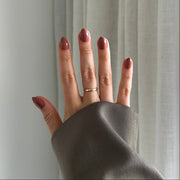 Hand with press on nails on wearing a gold ring against a neutral background