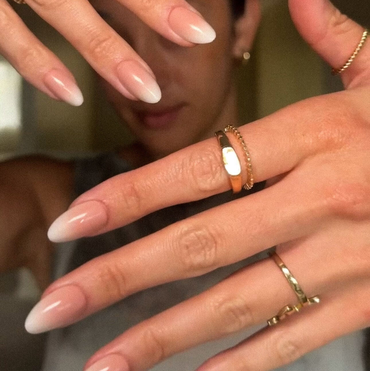 Close-up of hands with long nails and multiple gold rings.