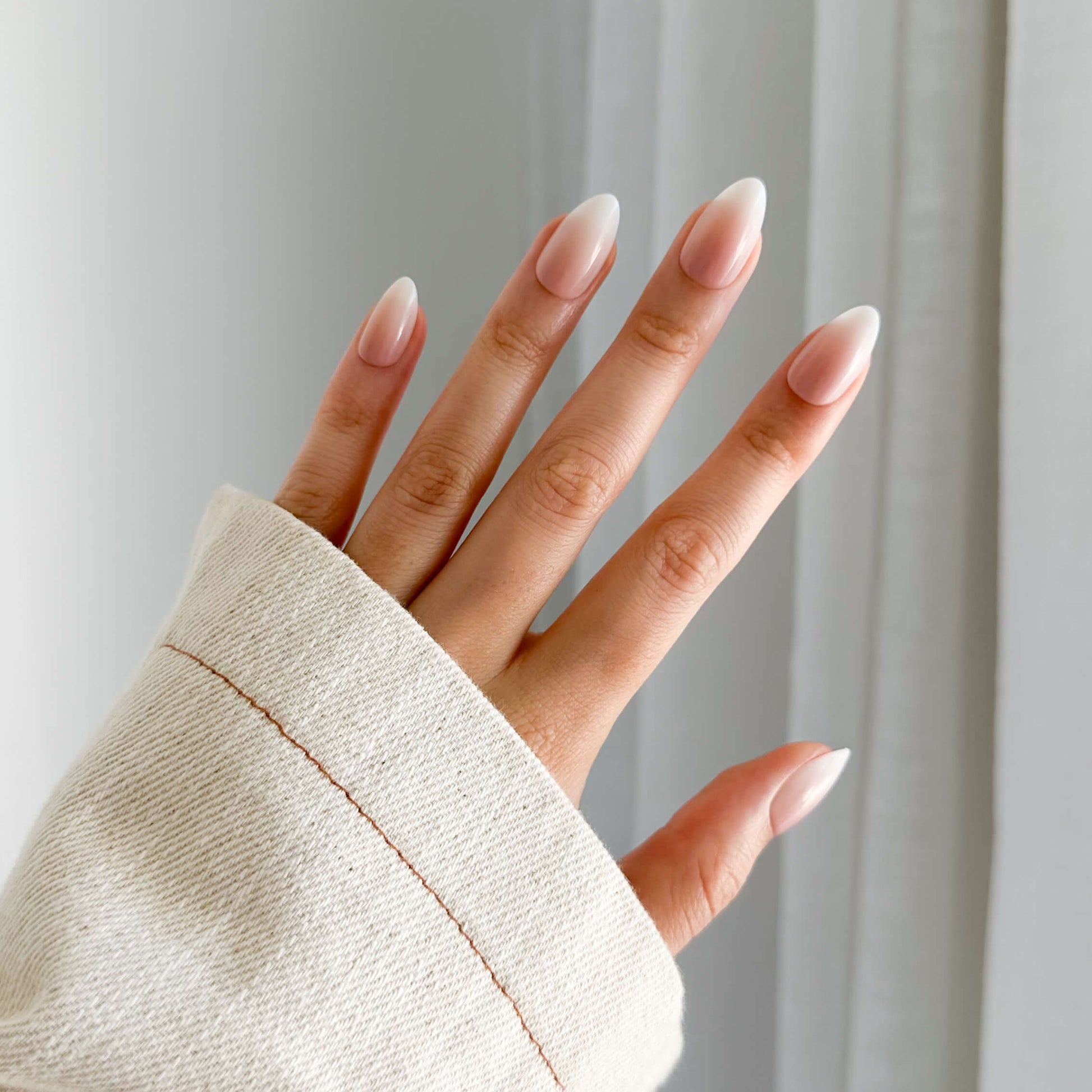 Hand with Almond ombre press on nails wearing a beige sleeve against a white background