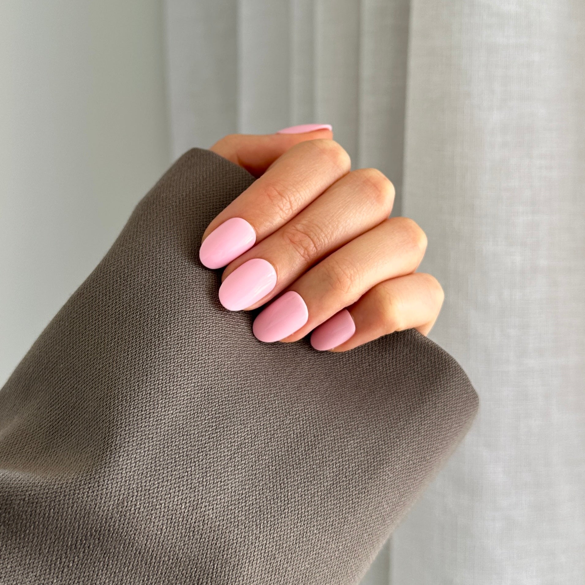 A hand with pink oval-shaped gel press on nails on a neutral background with a grey sleeve.