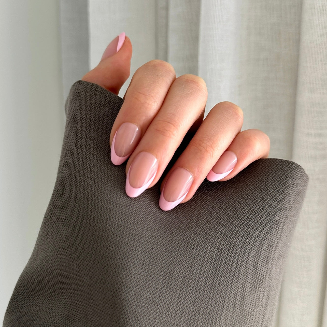 Hand with pink tip press on nails on a white textured surface