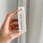 A hand holding a bottle of 'pressing nails. NAIL GLUE REMOVER' against a light background.