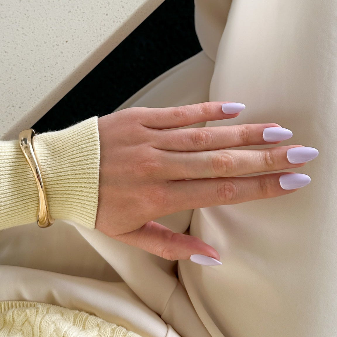 Close-up of a hand with light purple press on nails on a white surface