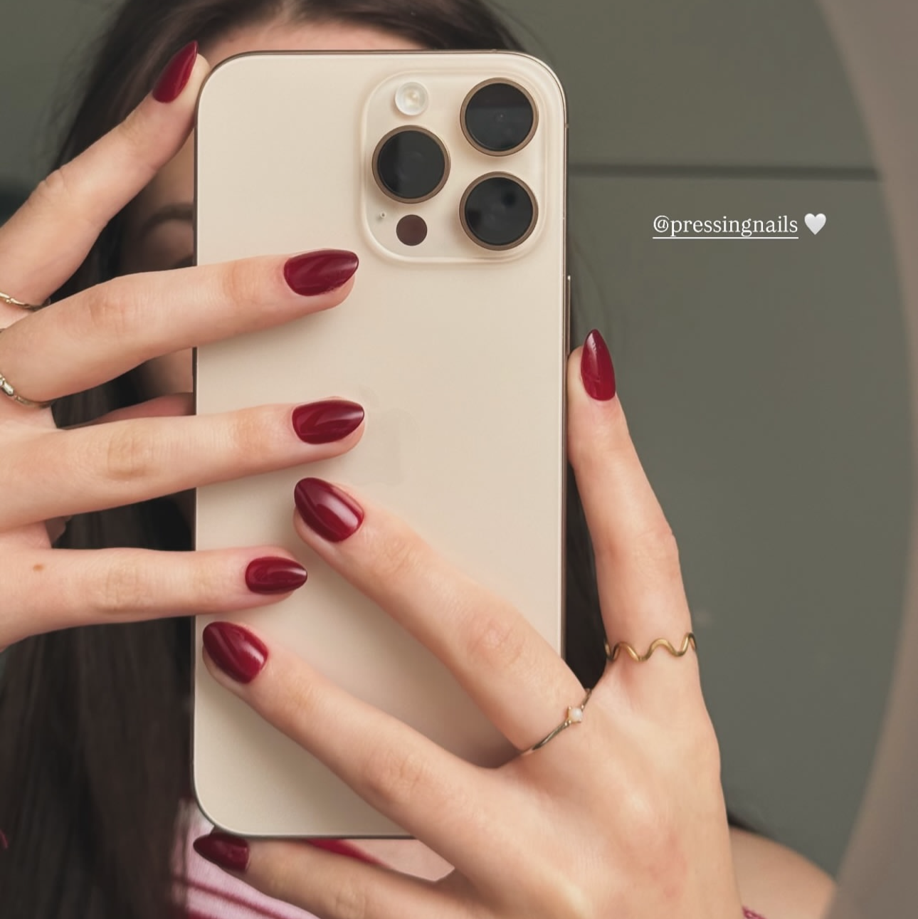 Person holding a phone with a mirror reflection, showing red press on nails and a ring.
