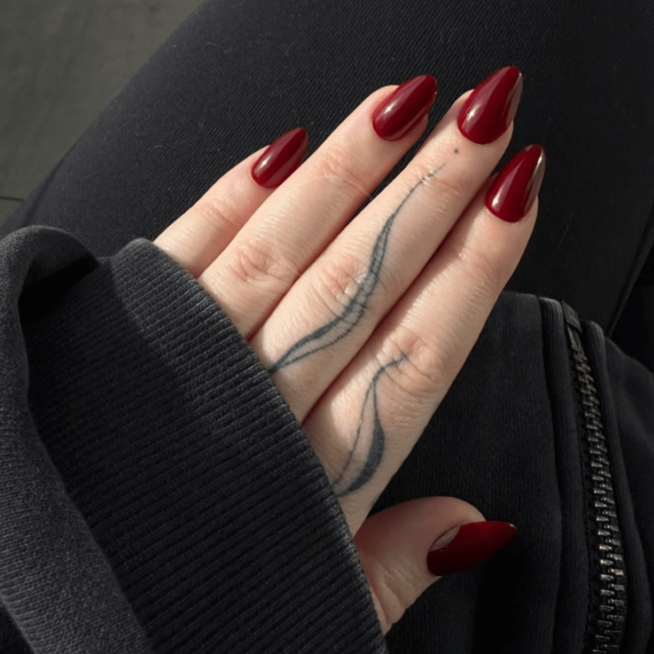 Hand with red press on nails and a tattoo on a dark background