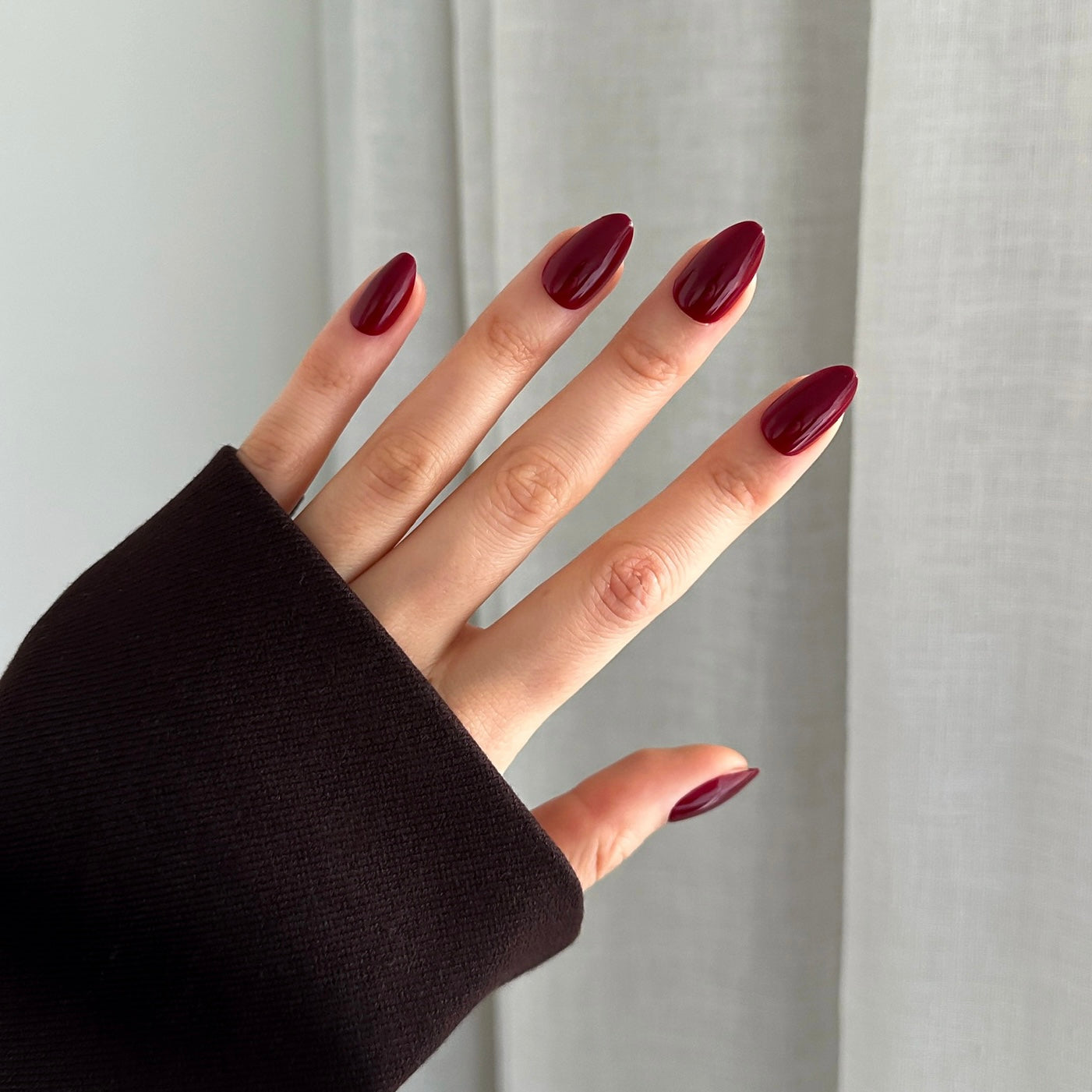 Hand with dark red press on nails against a neutral background
