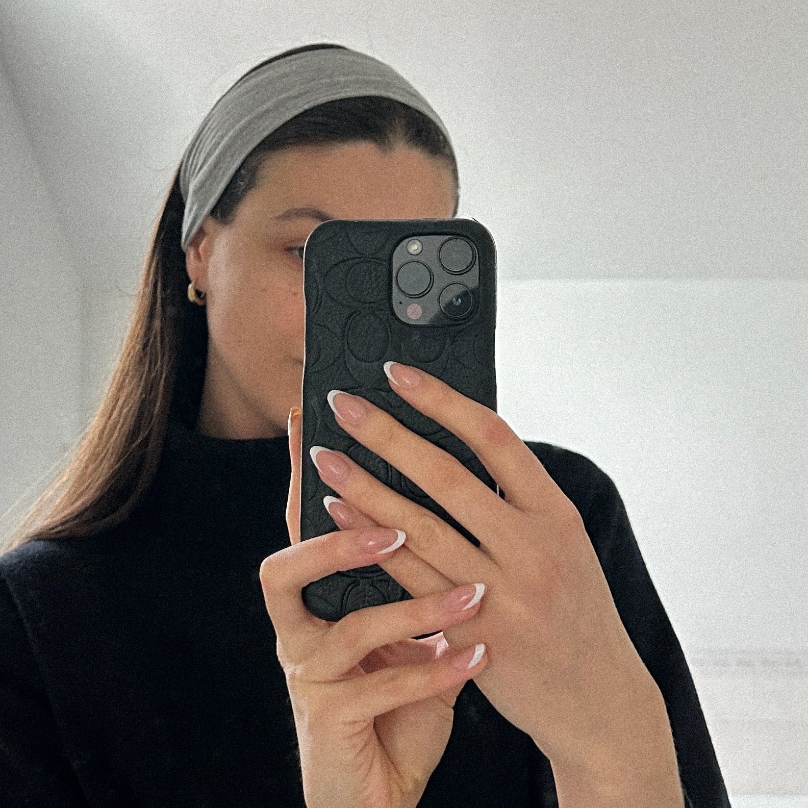 Person taking a mirror selfie in a bathroom wearing a black outfit and gray headband. Showing off pressing nails 