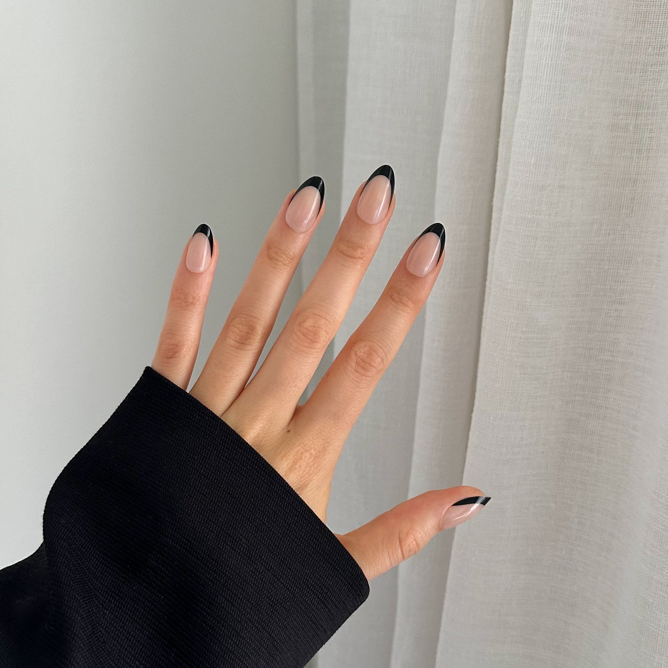 A hand with black-tipped gel press on nails, wearing a black sleeve.