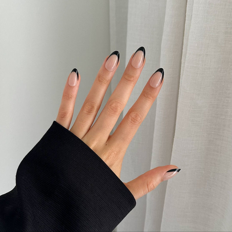 A hand with black-tipped gel press on nails, wearing a black sleeve.