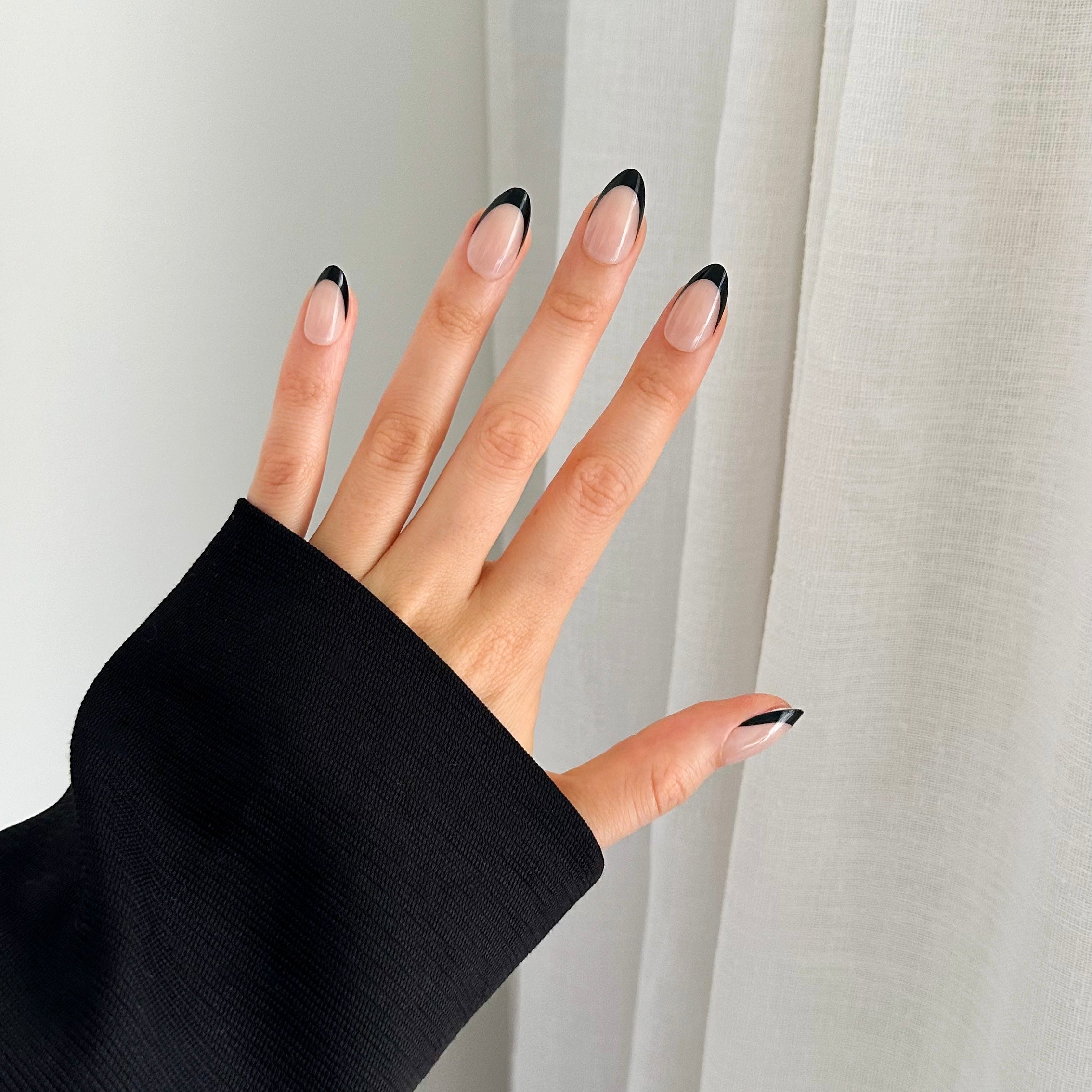 A hand with black-tipped gel press on nails, wearing a black sleeve.