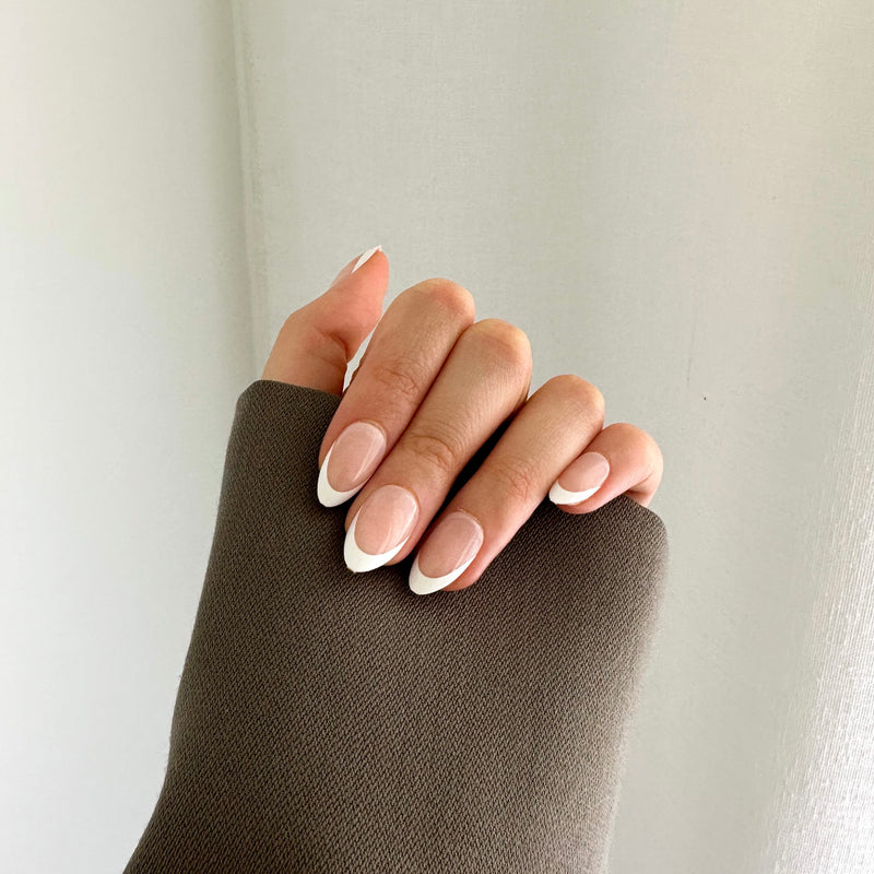 A hand with press-on nails featuring a white tip design.