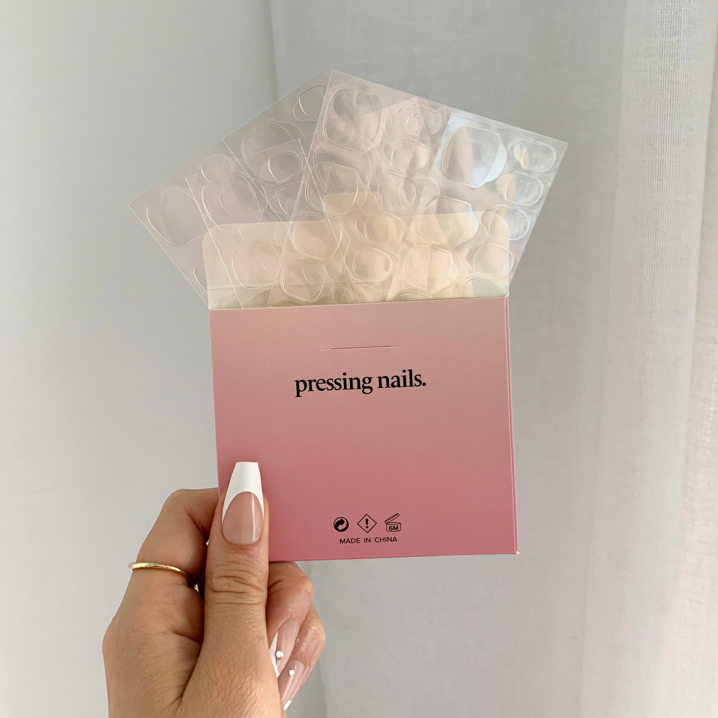 A hand holding a box of nail adhesive tabs with the brand name 'pressing nails' visible on the packaging.